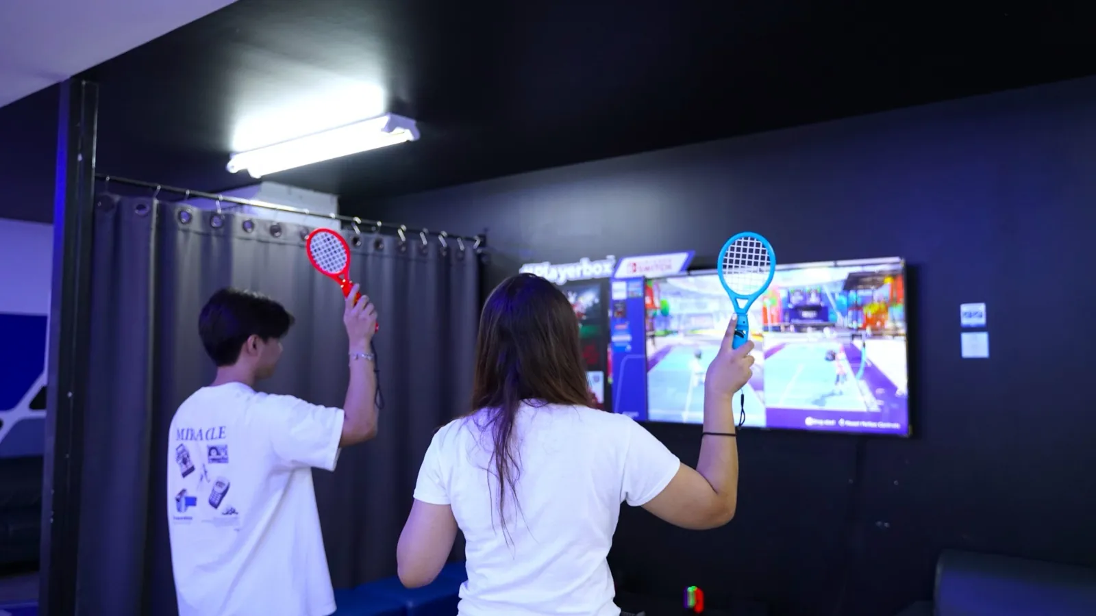 Two players swinging racket controllers at Nintendo Switch tennis at Chula 28