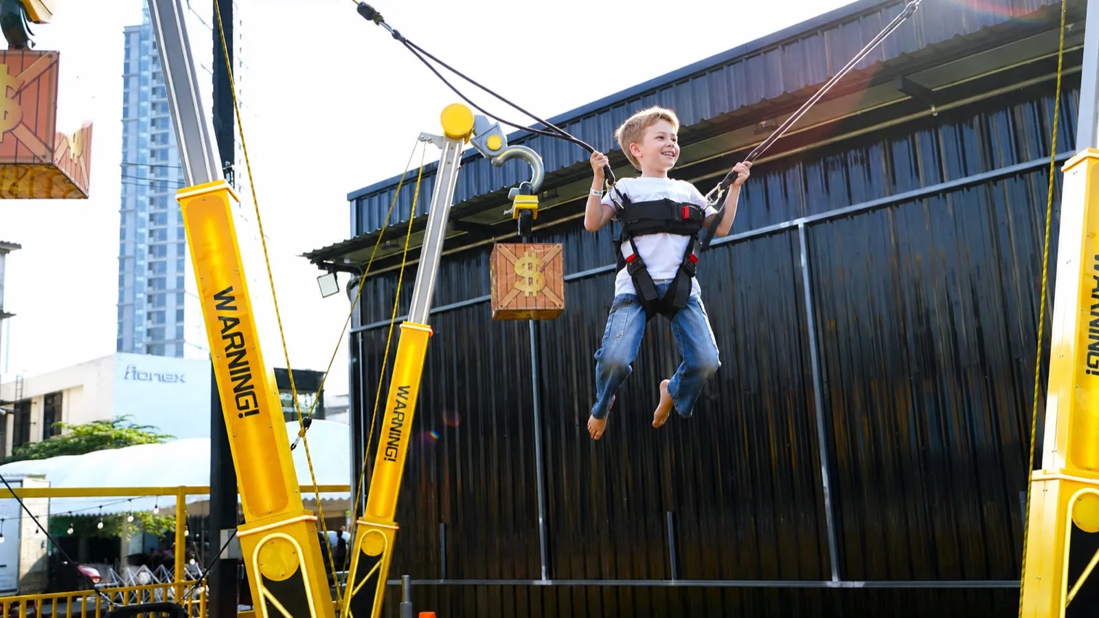 Boy bouncing on the outdoor Sky Jumper rig with the Bangkok skyline behind at Chula 28